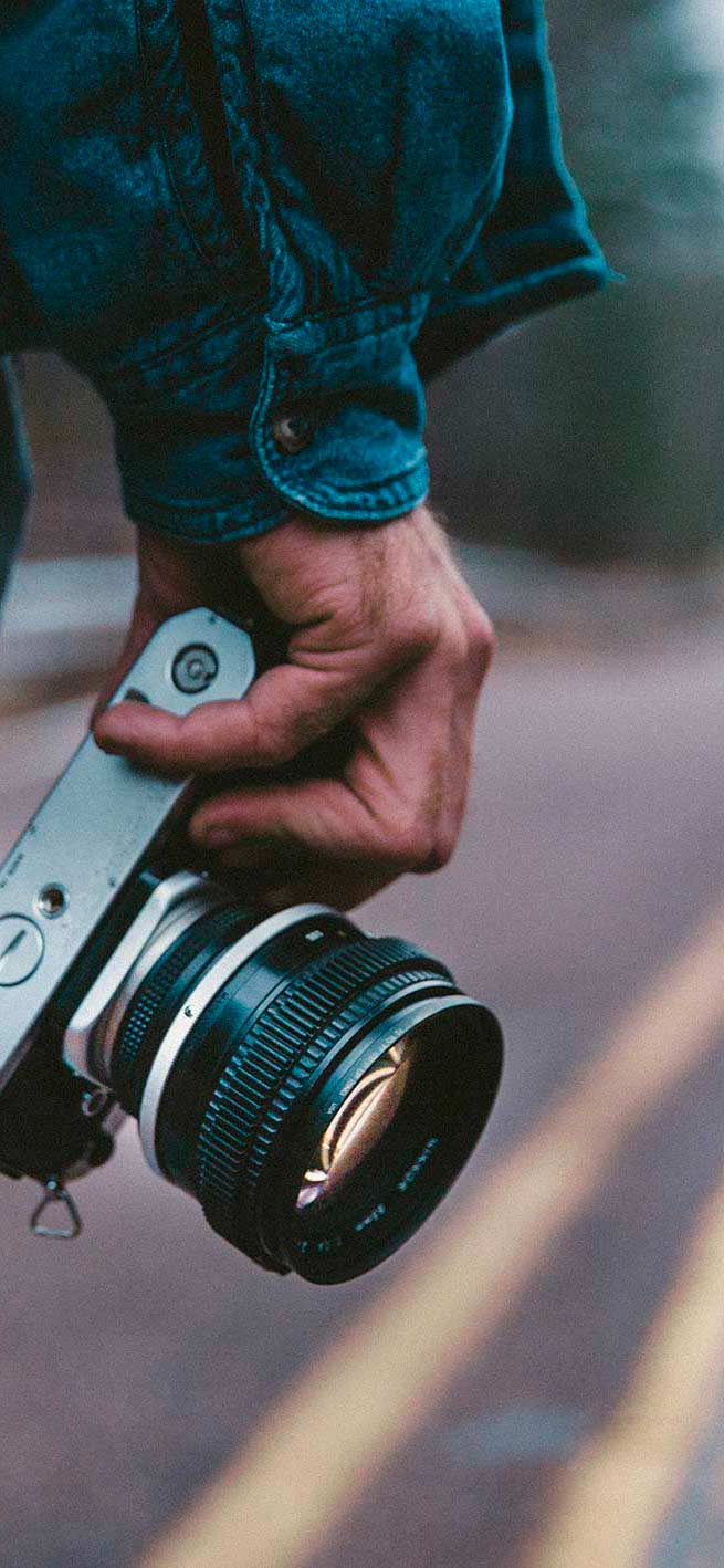 Man holding a camera in his right hand and standing in the middle of a deserted double lane highway in the countryside